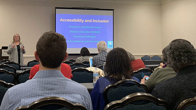Woman giving a presenting about Accessibility and Inclusion to an audience of attendees in an event room